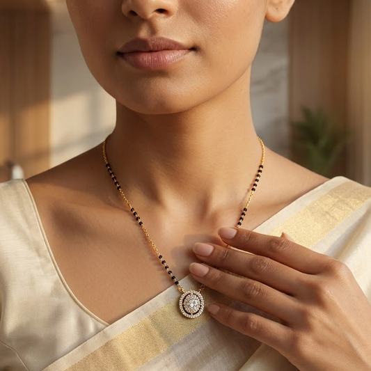 A woman wearing a cream-colored sari and a beaded necklace with a round pendant, posed in a softly lit indoor setting.